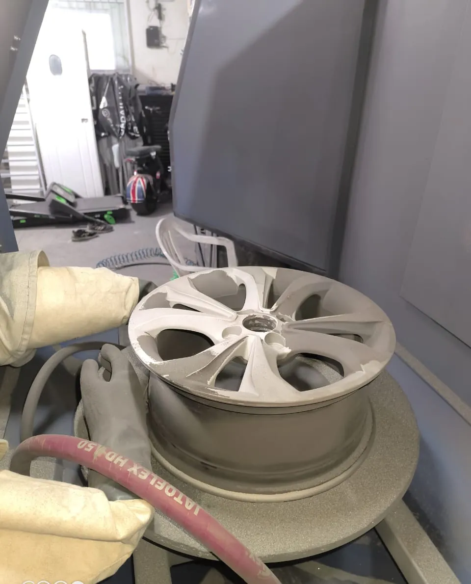Roda automotiva sendo jateada dentro de um gabinete de jateamento