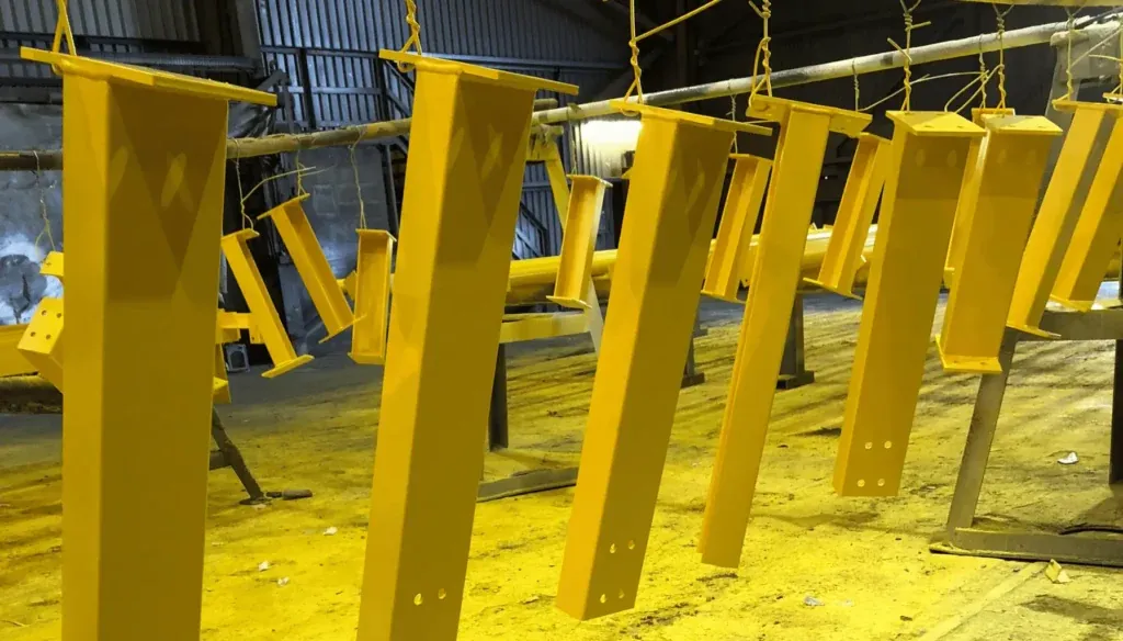 Peças metálicas recém-pintadas de amarelo, suspensas em uma linha de pintura industrial