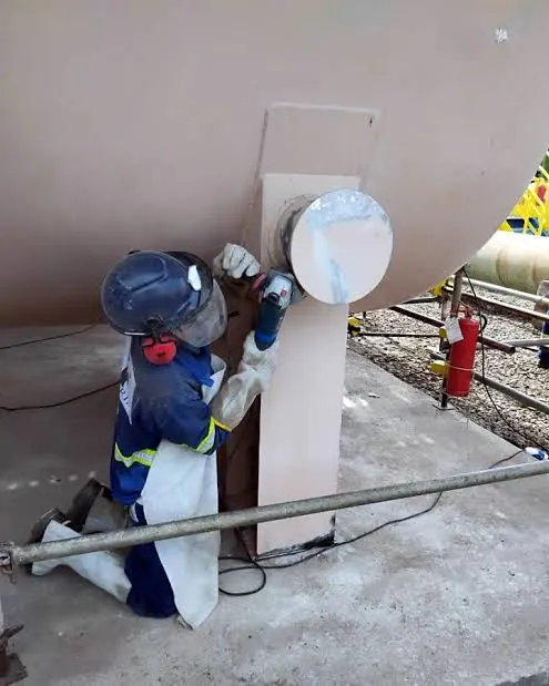 Operador com equipamento de proteção preparando a superfície de um equipamento metálico