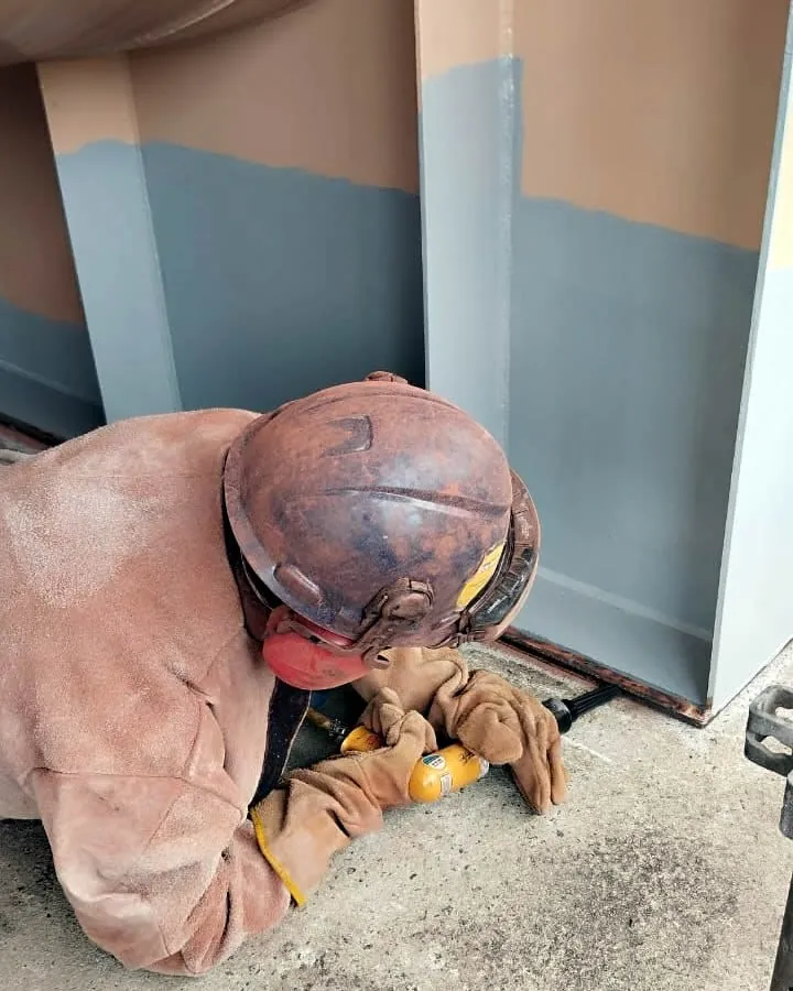 Operador preparando a superfície metálica junto a uma parede já revestida